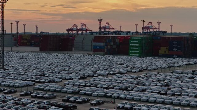 Panoramic view of thousands of white cars parked at port vehicle terminal at sunset