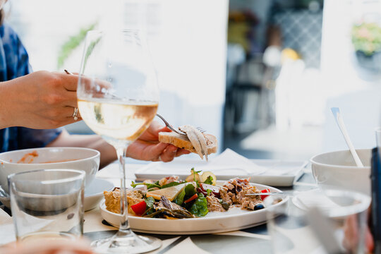 A person's hand spreads a tasty local appetizer onto a slice of fresh bread at a sunny outdoor restaurant. Enjoyable Mediterranean dining and authentic food lifestyle concept.