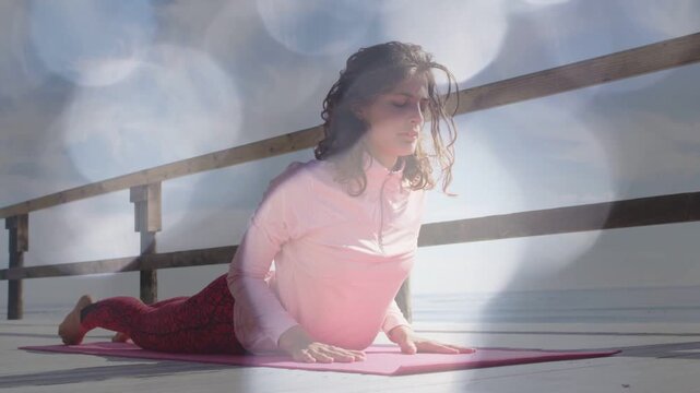 Woman doing yoga on pink mat pressing palms and rising to backbend opening chest lensflare drifting