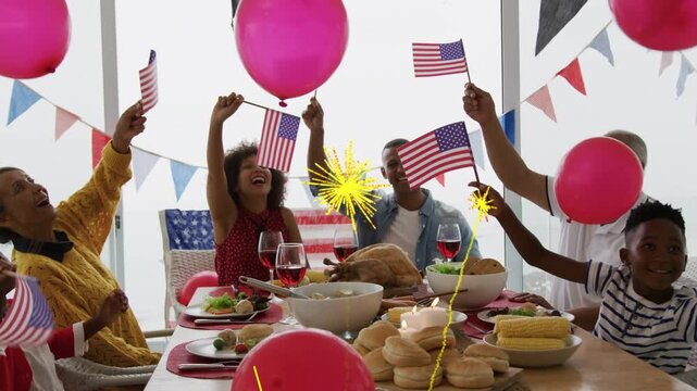Family celebrating at table, waving flags, lifting balloons, sparks hiding faces for marketing
