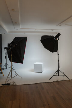 Professional photo studio setup with white cyclorama wall, softbox lighting equipment, and a white podium cube. Empty space for product photography or fashion shoots in a modern studio.