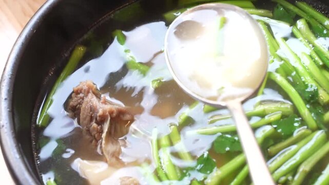 Spoon stirring galbitang broth containing water parsley and beef