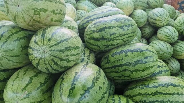 Closeup view of fresh watermelons stacked together showing green rind texture and ripeness