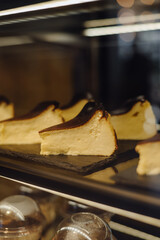 Obraz premium Slices of San Sebastian burnt cheesecake on a dark display shelf in a cafe. Creamy Basque dessert with a caramelized top, perfect for restaurant menus and food photography.