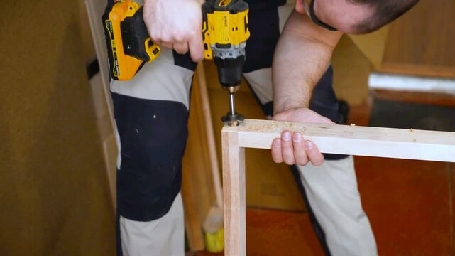 A man with works in his workshop. Profession carpenter. A man works with a tree. The carpenter takes drills holes wooden products in a bright workshop. Carpentry, craftsmanship, handwork concept.