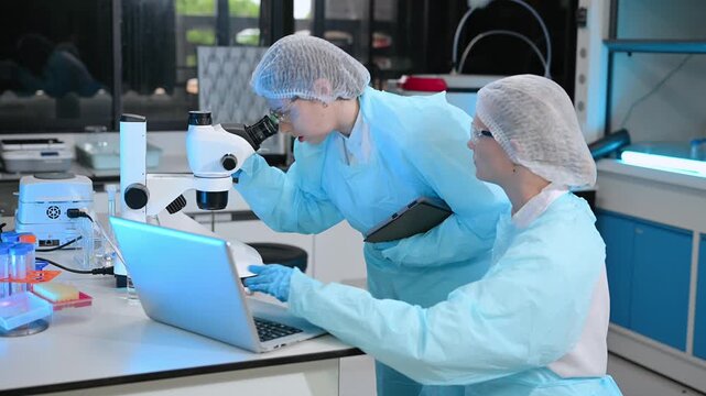 Two scientists working together in advanced laboratory using microscope and pipette for biotechnology, medical testing