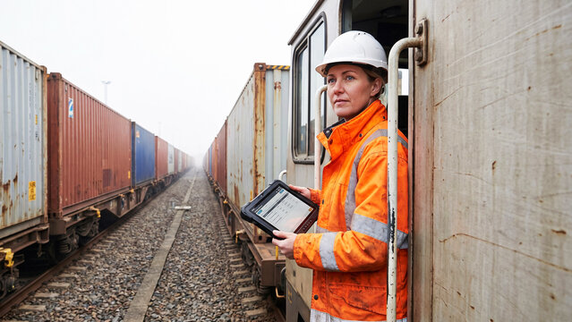 Female Freight Train Conductor in Hi-Vis Jacket Holding Industrial Tablet at Remote Rail Siding with Container Wagons, Rail Freight, Supply Chain, Logistics, Cargo