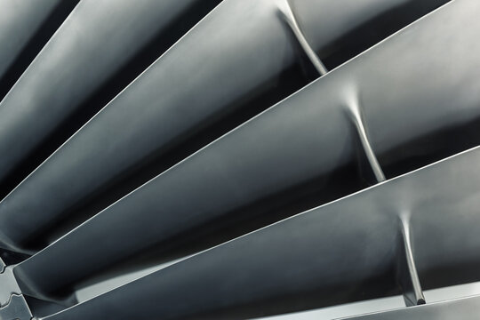 Closeup detail view of jet turbine blades with metallic texture and geometric symmetry. Modern aerospace engineering background with abstract industrial pattern, dark tones, precision and power