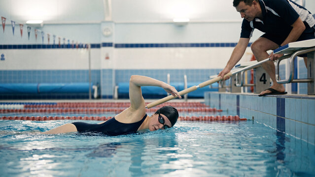 Visually Impaired Female Swimmer Doing Front Crawl in Indoor Pool with Tapper Coach at Lane End, Adaptive Sport, Inclusive Sport, Paralympic Style Training, Para Swimming