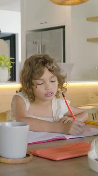 Vertical video: Fidgeting kid in dress after cue, writing in notebook at home with red pencil