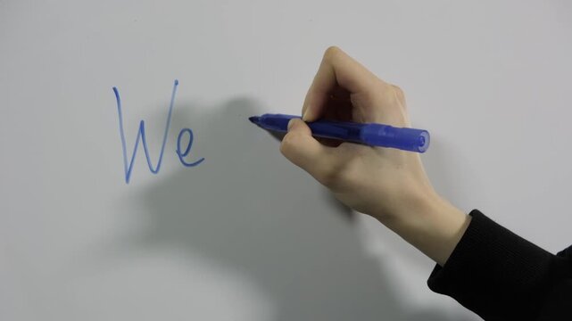 Close-up of a hand writing the word 'we need to focus on' with a blue marker on a white board
