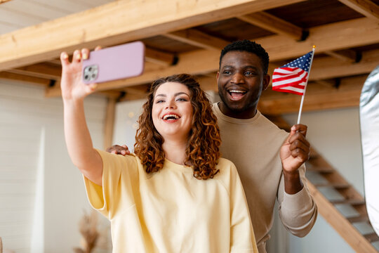 Diverse couple smiling, taking selfie with American flag