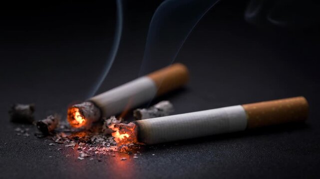 Close-up of two burning cigarettes with glowing embers and smoke on dark surface highlighting smoking and tobacco use