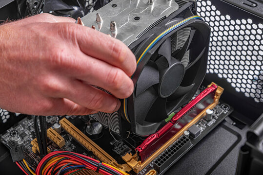 A person's hand is shown installing a large CPU cooler onto a motherboard inside a desktop computer case.