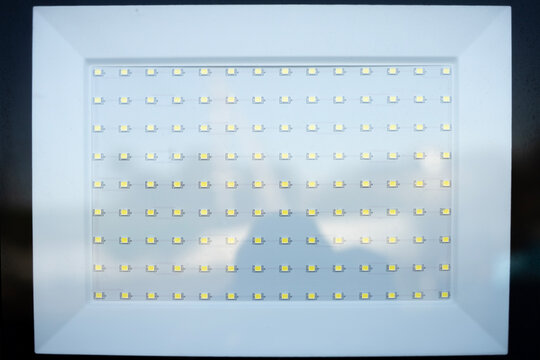 Close up of rectangular LED floodlight panel with rows of light emitting diodes inside white frame, showing electrical lighting equipment.