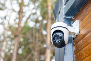 Outdoor security camera mounted on wooden house wall in forest, close surveillance detail. Concept: home security © Marya