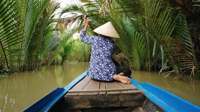 Vietnam woman in traditional boat through lush mekong delta jungle for a tour