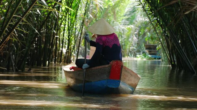 Vietnam woman sailing at boat on mekong river delta through lush jungle canal on a sunny day
