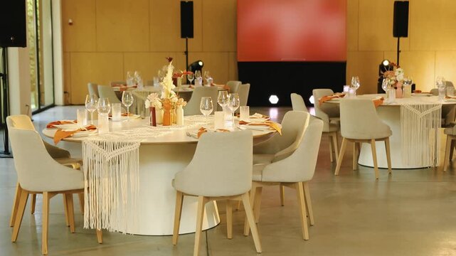 Boho and rustic wedding decor in empty banquet hall in slow motion. Decorated round tables and chairs inside marriage celebration venue with wooden panels. Cinematic 4K slowmo video.