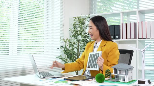 Smiling businesswoman presenting a wind turbine model with ESG and net zero reports, promoting renewable energy and sustainable business solutions in a modern office.