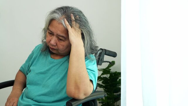 Lost in Thought: A portrait of elderly woman with gray hair sits in a wheelchair, head in hand, expressing a moment of contemplation, sadness, or concern.