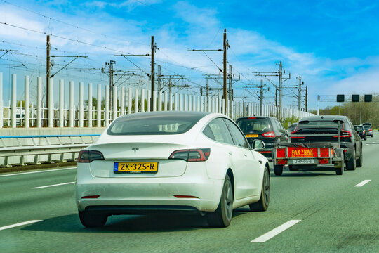 Netherlands - April 17, 2026: Sustainable transportation and electric mobility on a Dutch highway featuring a Tesla Model 3 and Volvo EV alongside electrified railway infrastructure near Amsterdam.