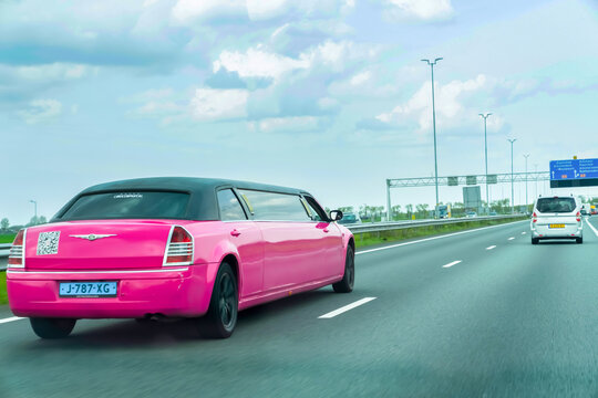Netherlands - April 17, 2026: A striking pink stretch limousine drives along a Dutch highway during daytime, captured in motion against a backdrop of road infrastructure and a cloudy sky.