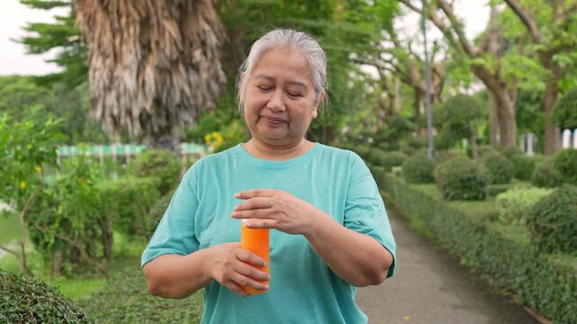 Healthy Senior Enjoying Juice: A serene senior holds a glass of freshly squeezed orange juice. She finds joy and a sense of wellness within the lush outdoors.