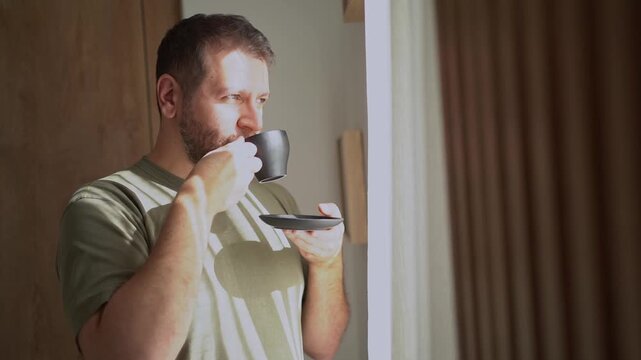 Contemplative bearded man drinking coffee by the window