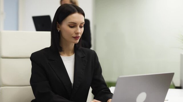 Businesswoman at office desk working on computer and engaging with camera. Concept corporate communication and professionalism.
