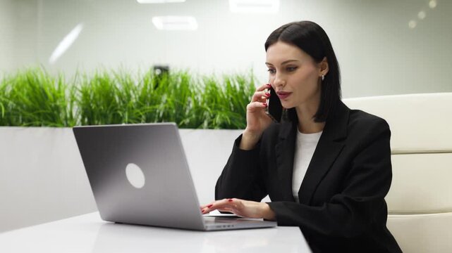 Office businesswoman speaking on smartphone and working with information on computer. Concept data processing and customer support.
