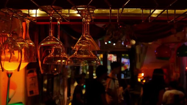 Wine glasses hanging upside down from bar ceiling rack with live music band performing in bokeh background at night