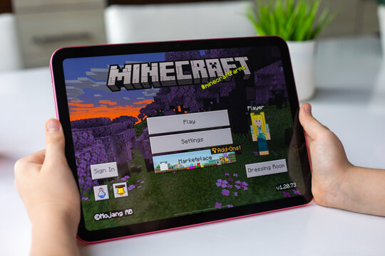 Children hands holding Apple iPad with multiplayer online game Minecraft mobile in the screen IOS phone. Games Minecraft was created by the Mojang Studios