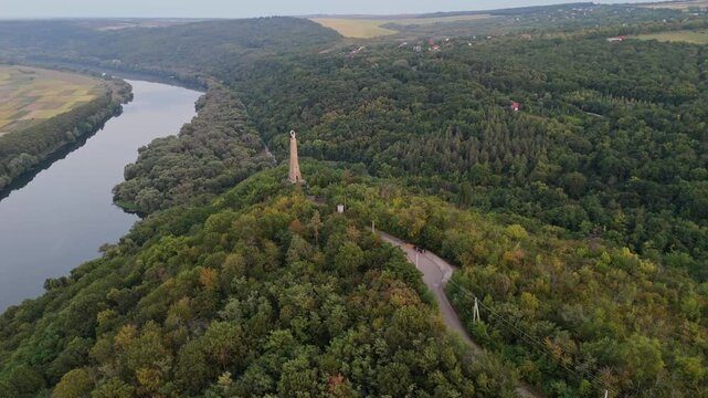 Scenic aerial shot of the Thanksgiving Candle monument in Soroca, Moldova. Cinematic drone flight showcasing the tall landmark on a lush green hilltop overlooking the Dniester River.