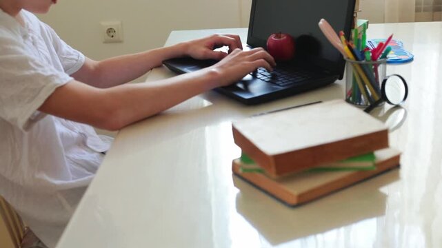 Student boy typing on laptop at desk with books, apple and stationery, back to school and e-learning concept, online education, homework