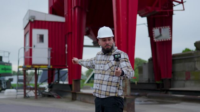 Industrial blogger in a hard hat vlogging with an action camera at a construction site while explaining project details