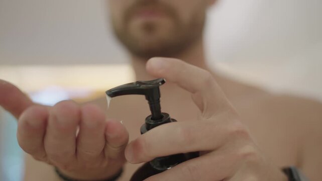 Shirtless man's hands pumping cosmetic moisturizing lotion from a black dispenser bottle