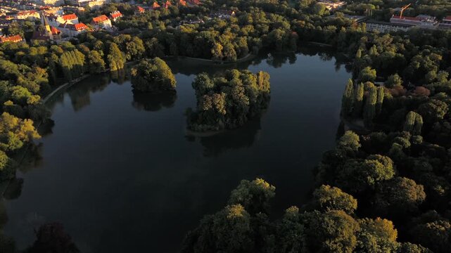 Luftbild Kleinhesseloher See im Englischen Garten, Munchen. Kuenstlicher See mit Inseln, umgeben von Baeumen, Wiesen und Biergarten. Beliebter Ort fuer Erholung und Reisen.