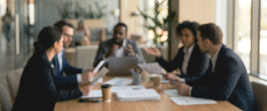 A diverse group of business professionals engaged in a meeting around a conference table, discussing documents and ideas in a modern office setting.