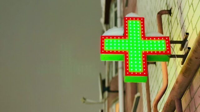 Neon green pharmacy cross signboard mounted on brick facade at dusk, glowing diode lights with red border, metal bracket