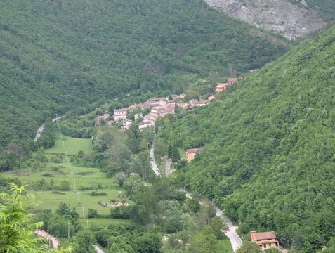 Borgo immerso in una valle verde, circondato da colline boscose e attraversato da una strada sinuosa. Atmosfera rurale, tranquilla e autentica, tipica dei paesaggi dell&rsquo;Italia Centrale