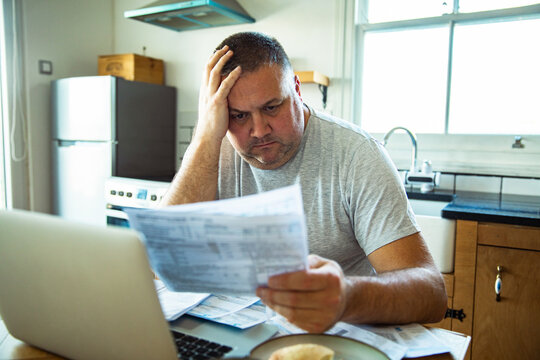 Stressed man reviewing household bills at kitchen table