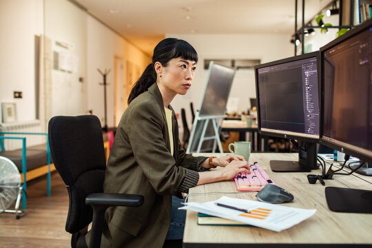 Woman software developer coding on dual monitors in modern office