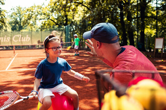 Coach high fives child during tennis lesson on outdoor clay court