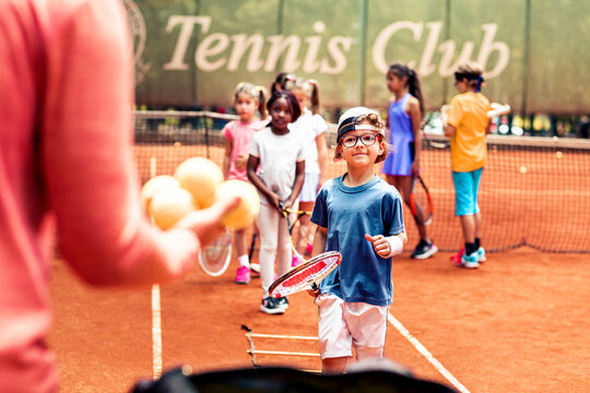 Children learning tennis with coach at clay court club