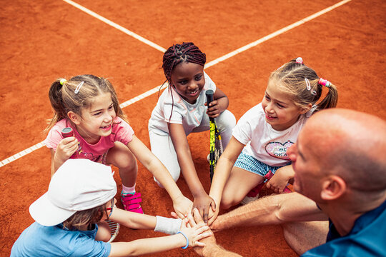 Children huddling with tennis coach on clay court