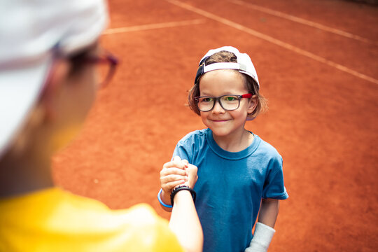 Smiling boy shakes hands on clay tennis court