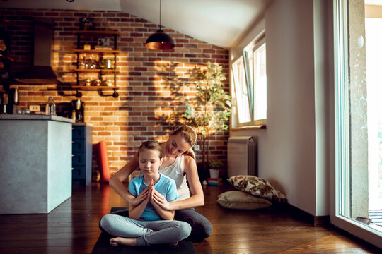 Mother and daughter meditating in a sunlit home living room