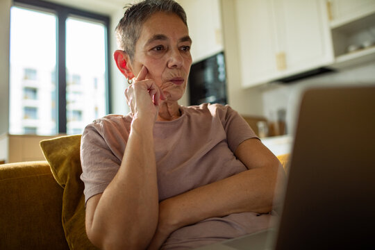 Thoughtful senior woman using laptop at home