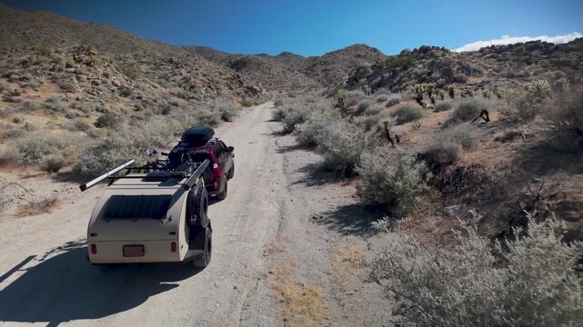 Aerial views show an SUV towing a teardrop camper trailer on a dirt trail in Anza Borego Desert State Park in California.